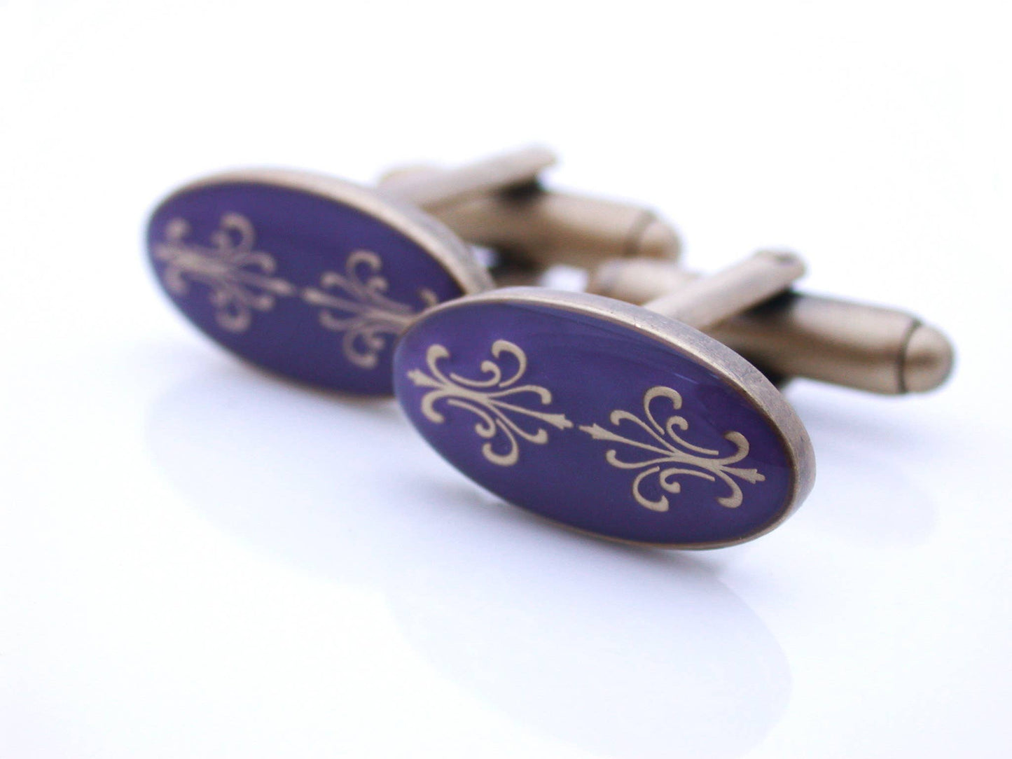 Antiqued gold oval cufflinks with two fleur de lys back to back on purple enamel